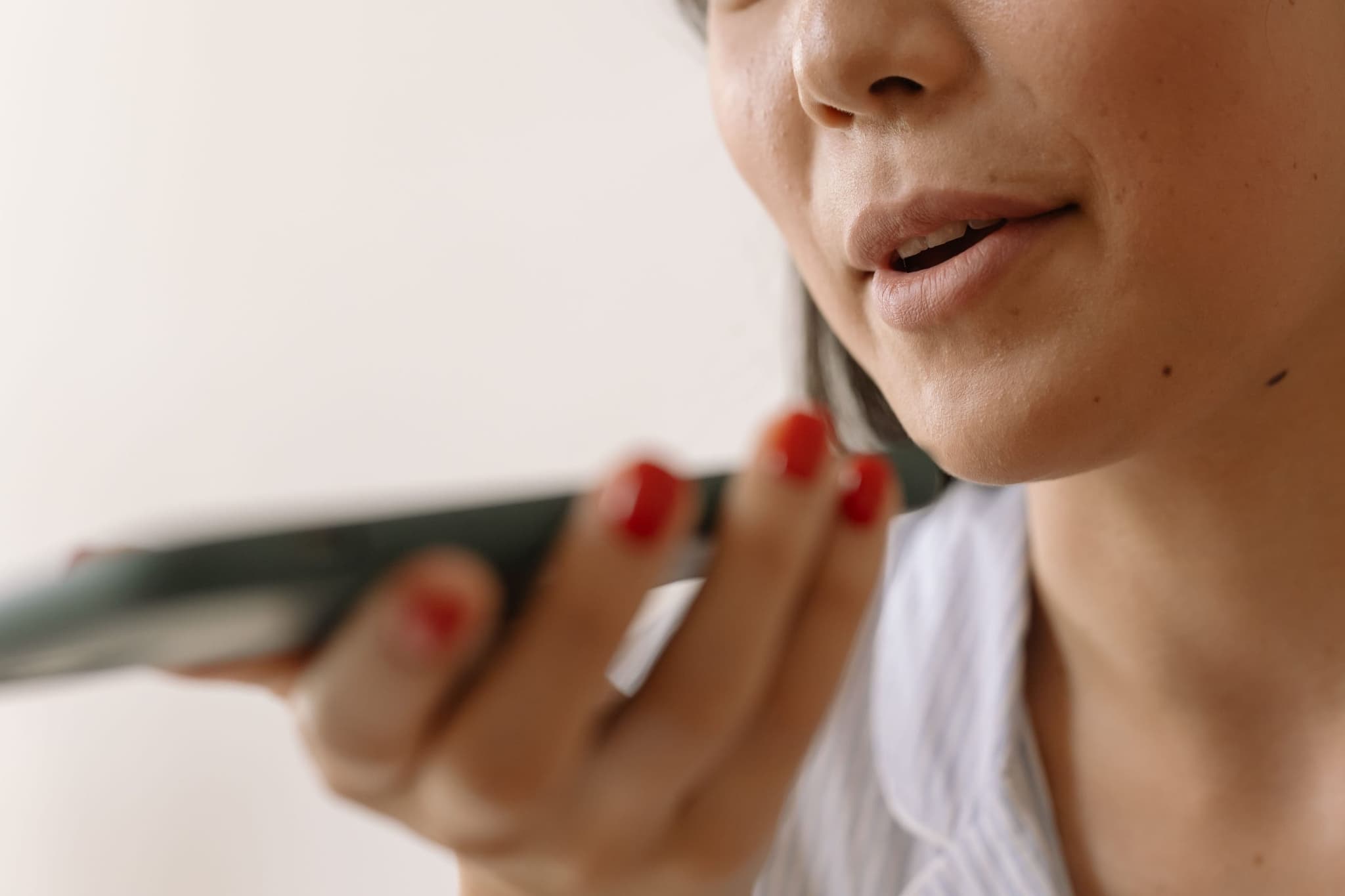 Mulher grava um áudio no celular, segurando o aparelho perto da boca.
