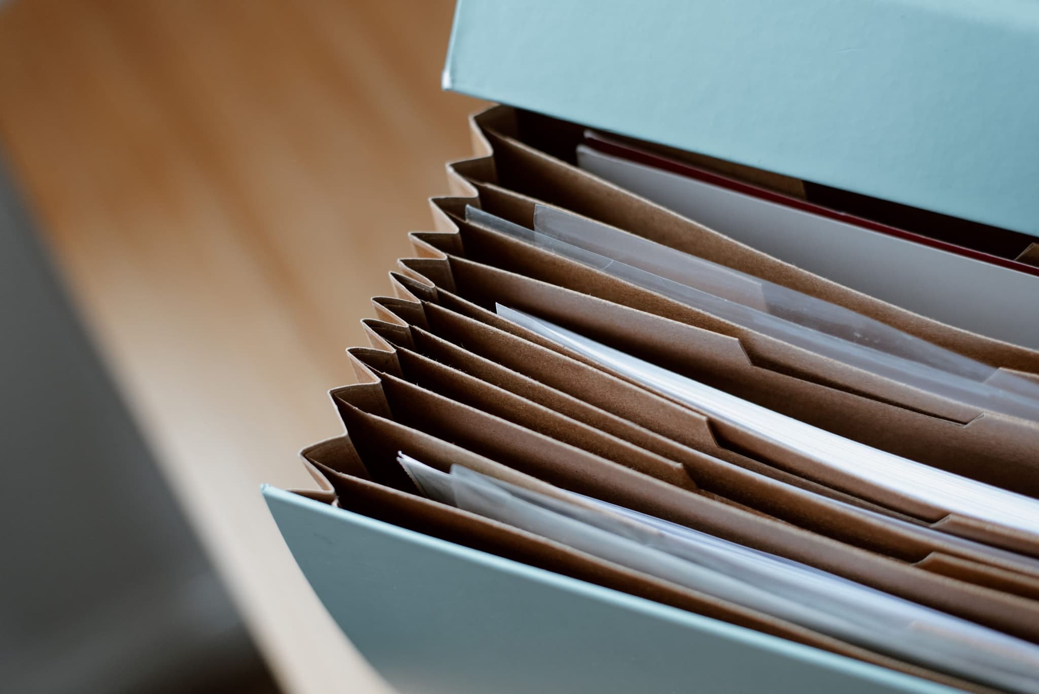 Pasta sanfonada aberta, com divisórias de papel pardo e folhas guardadas em ordem.
