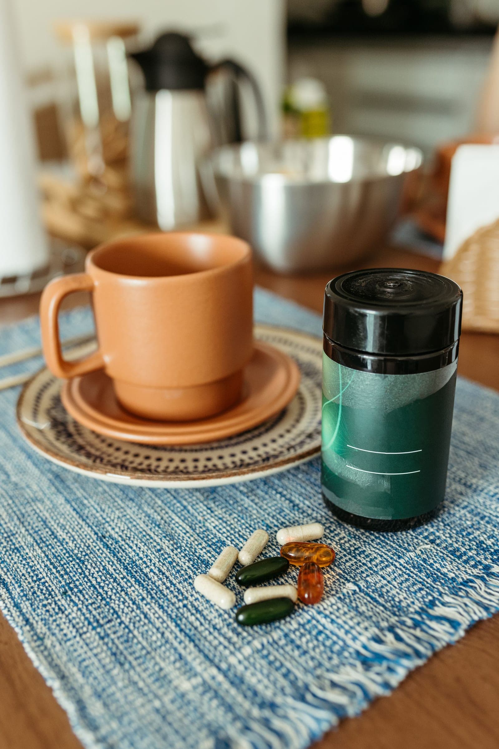 Cápsulas separadas sobre o jogo americano, ao lado de uma xícara de barro, na mesa do café da manhã, com uma garrafa térmica ao fundo.